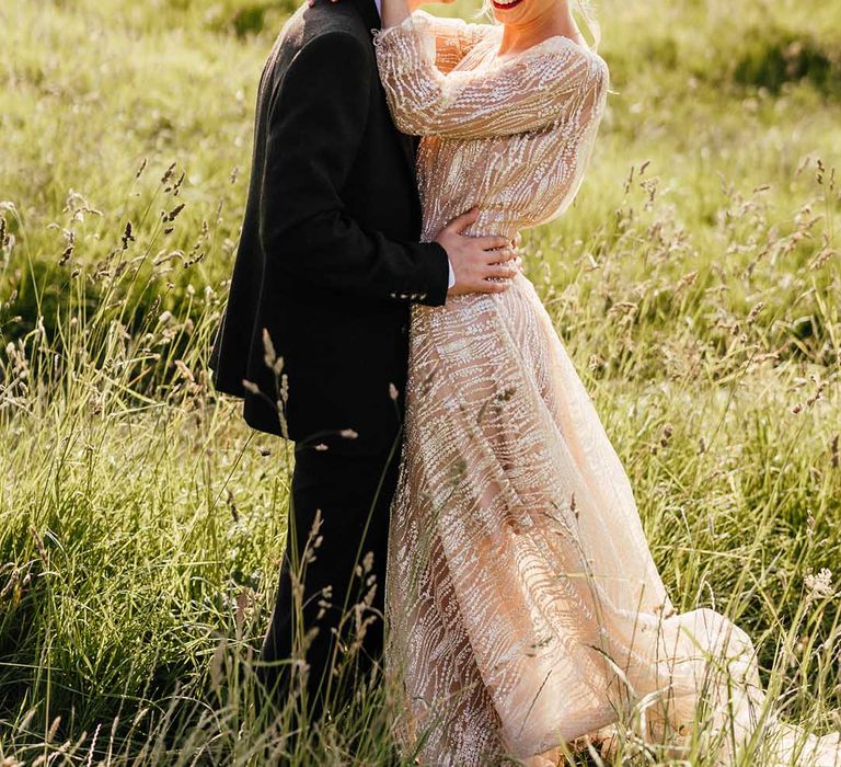 Bride & groom hold their arms around one another as the sun shines around them