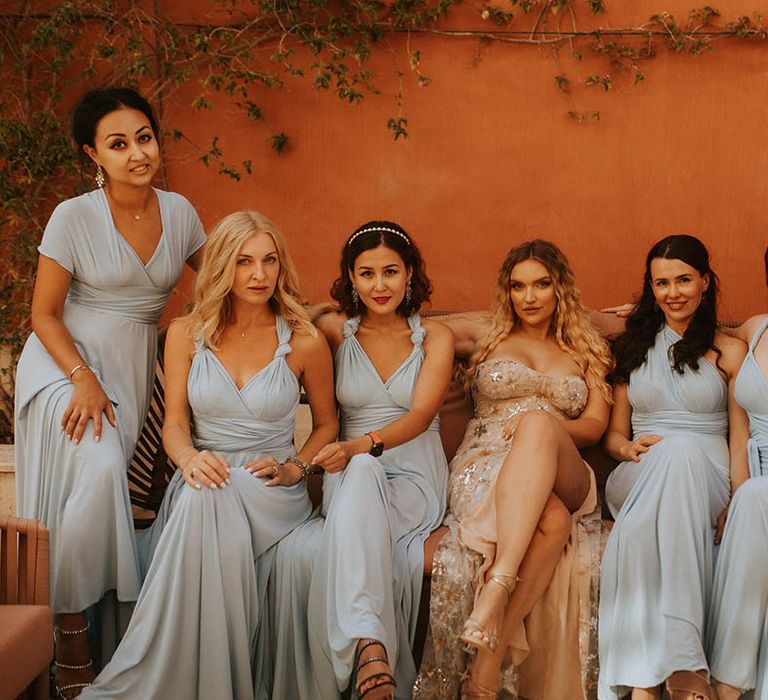 Bride sits with her bridesmaids who wear dusty blue gowns and bride wears dress with detachable skirt