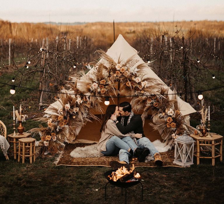 Boho campfire engagement session with bell tent, dried flowers, fire pit, and candles 