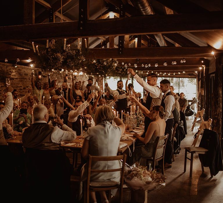 Rustic wedding at Dewsall Court with wedding guests raising their glasses during the wedding reception speeches 