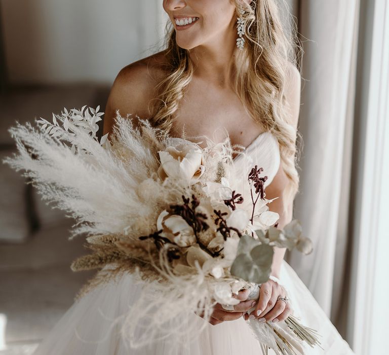 Bride holds dried pampas grass bouquet and wears her hair in loose curls with embellished head piece 