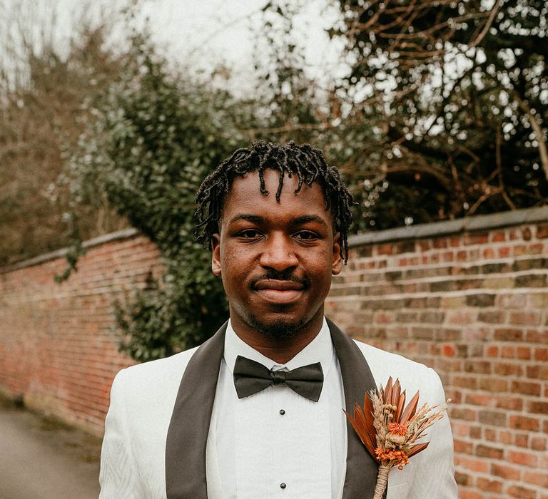 Groom in white tuxedo and orange buttonhole