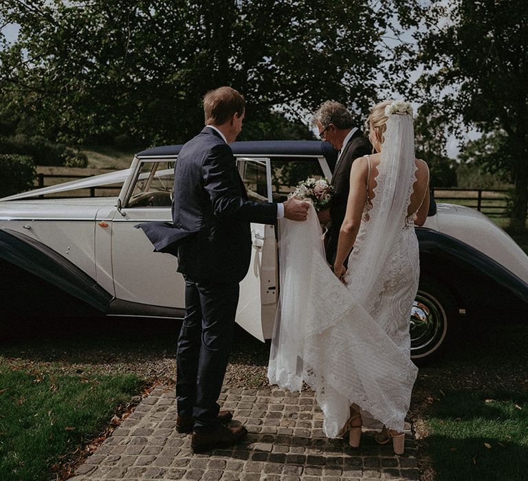 Bride enters vintage black and white wedding car wearing blush pink block wedding heels