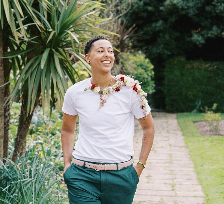 Transgender male in a white t-shirt, green chinos and flower collar 