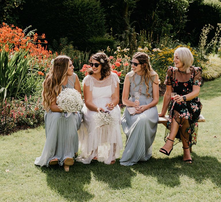 Bride in sunglasses sits with bridesmaids in green pleated dresses and wedding guest