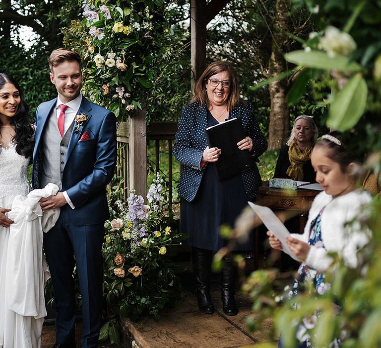 Bride and groom listen intently to young girl who performs a reading during the ceremony