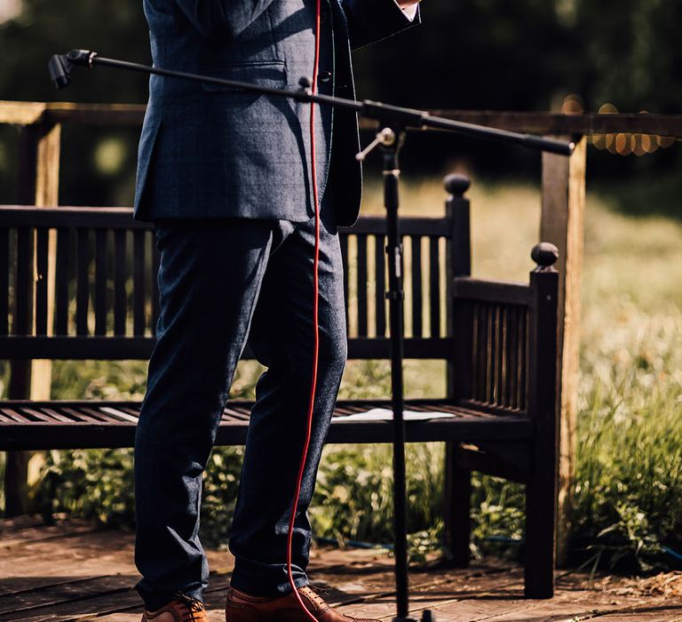 Groom in blue suit and sunglasses reads out his wedding speech 