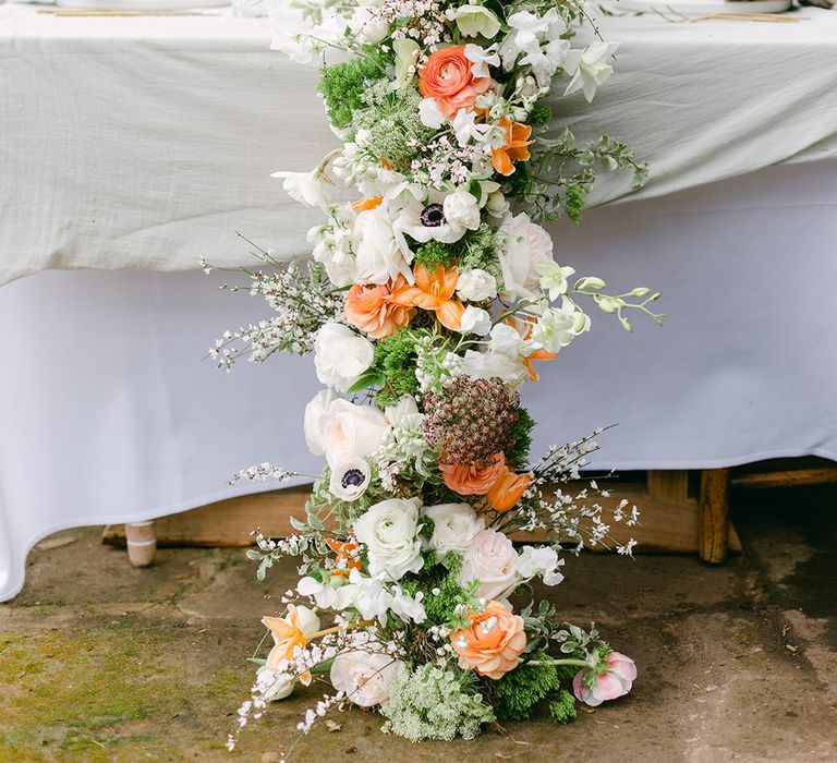 wedding flower table runner with green foliage and white and peach flowers including anemones, roses and ranunculus 