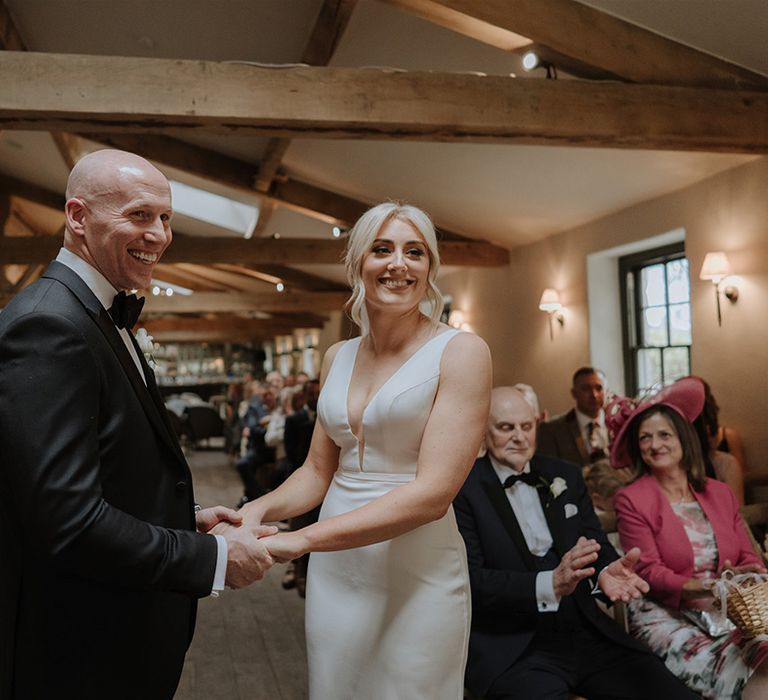 Bride and groom hold hands and smile at their wedding ceremony 