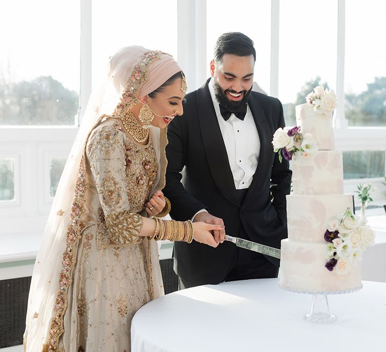 Bride & groom cut their four tier wedding cake during reception as groom wears black tie and bride wears traditional saree 