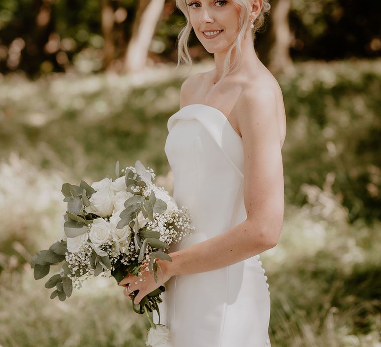 Traditional bride in a strapless gown holding a white rose bouquet with pearl earrings 