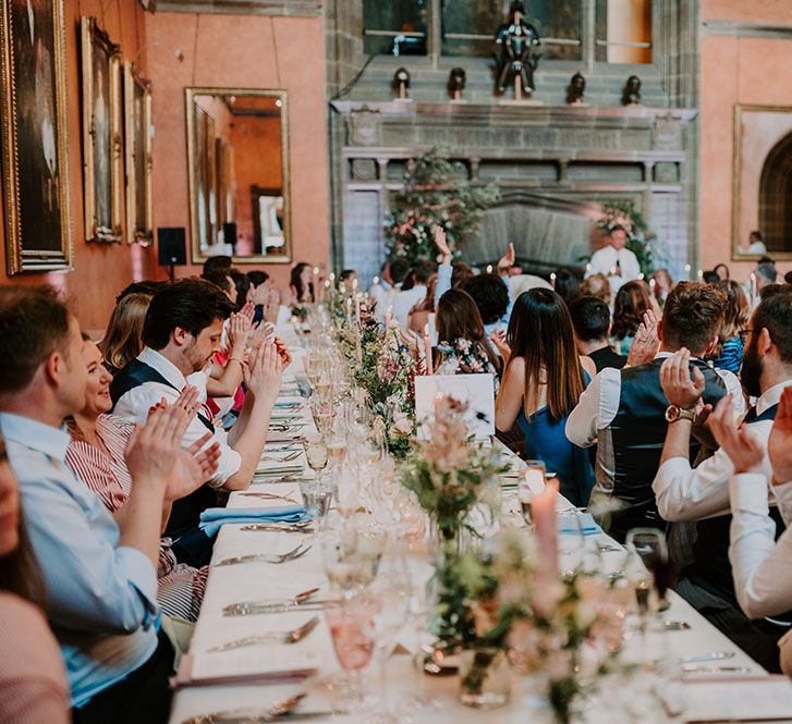 Banquet tables during wedding reception covered with white tablecloths and small pastel bouquets and pink pillar candles 