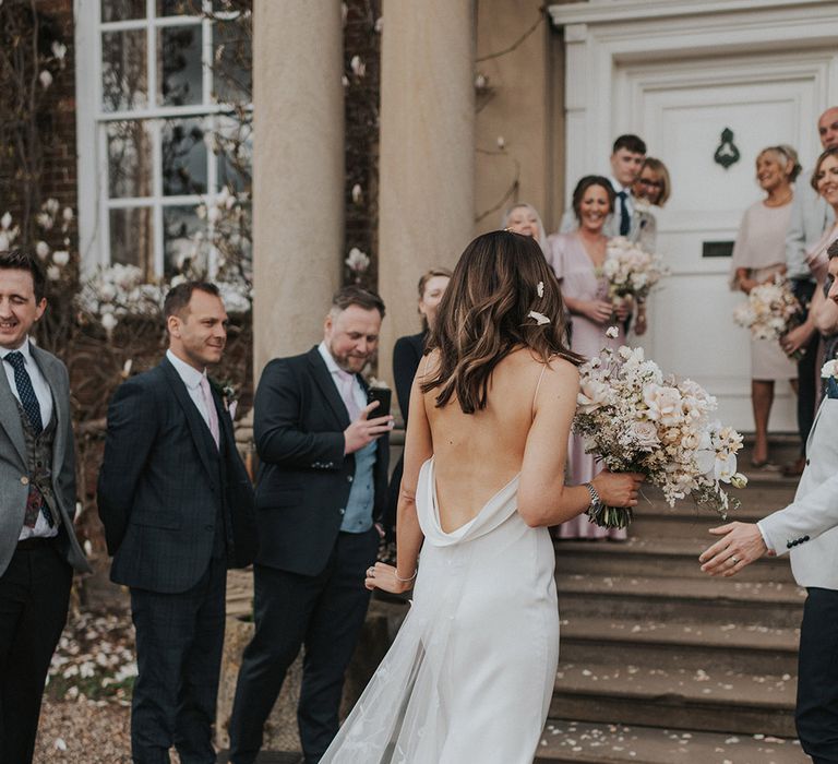 Wedding guests stand to take pictures of the bride and groom with the bride in a backless Alexandra Grecco wedding dress 