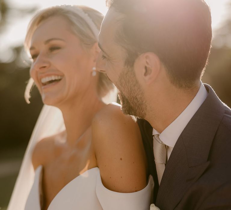 Bride wears Suzanne Neville wedding dress with plunge neckline whilst stood with her groom in the sunshine outdoors