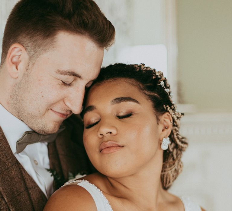 Groom in a brown wedding suit hugs the bride from behind in a sparkly plunging wedding dress