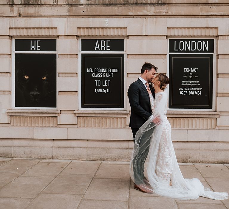 Bride wearing lace wedding dress kisses her groom outdoors on their wedding day 