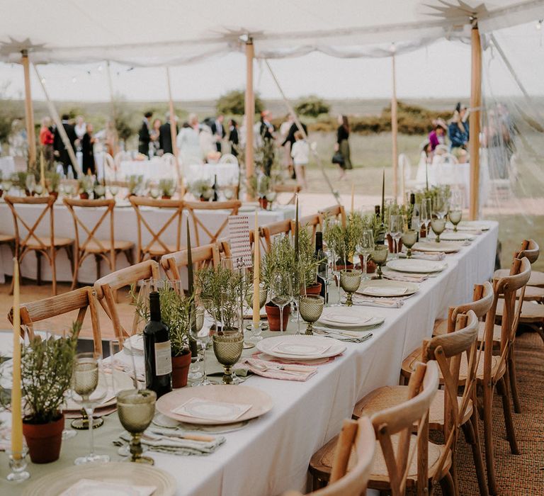 Yellow taper candles with sage green table runner and coloured glassware with wooden chairs for marquee wedding reception