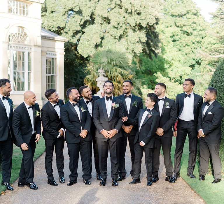 Groom stands with his groomsmen in black-tie complete with floral buttonholes and pocket squares 