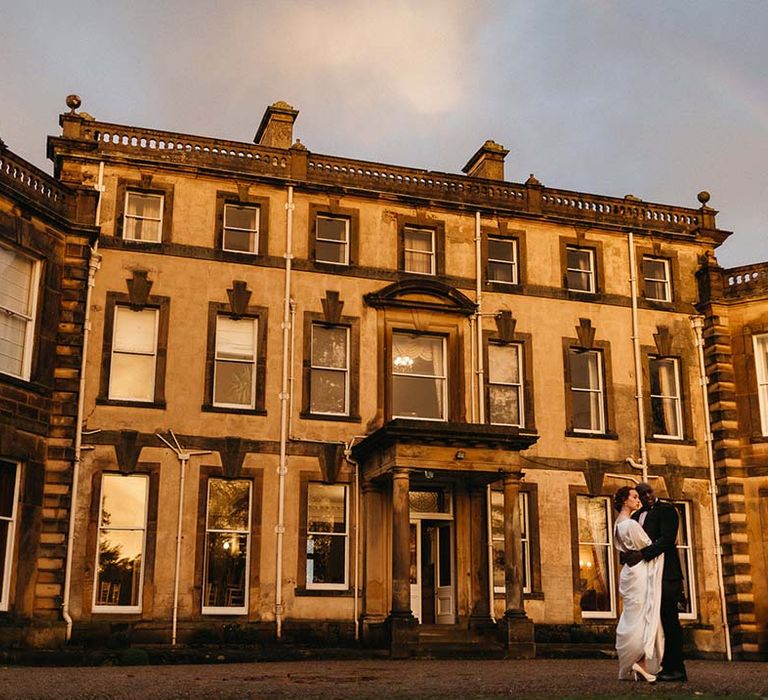 Bride and groom embracing outside Pepper Arden Hall at golden hour with rainbow 