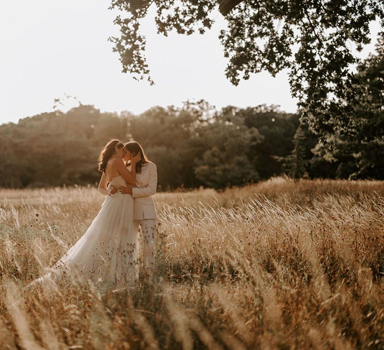 The brides share a kiss in a field during golden hour 