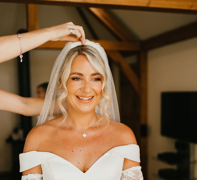 Blonde bride wears her hair in loose curls to the front and off-the-shoulder princess wedding dress with detachable lace sleeves 