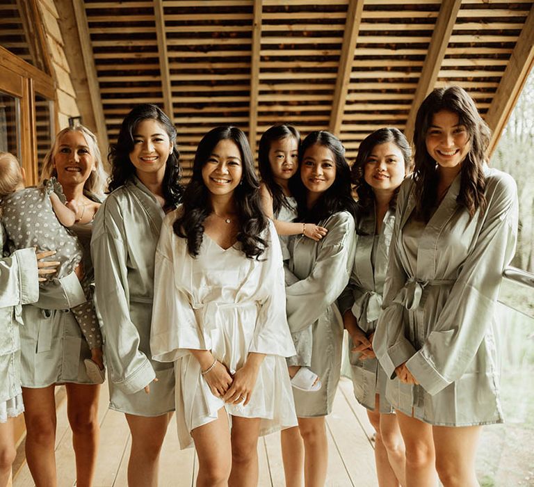 Bridesmaids in sage green satin robes with the bride in a white satin pyjama set as they get ready for the wedding day 