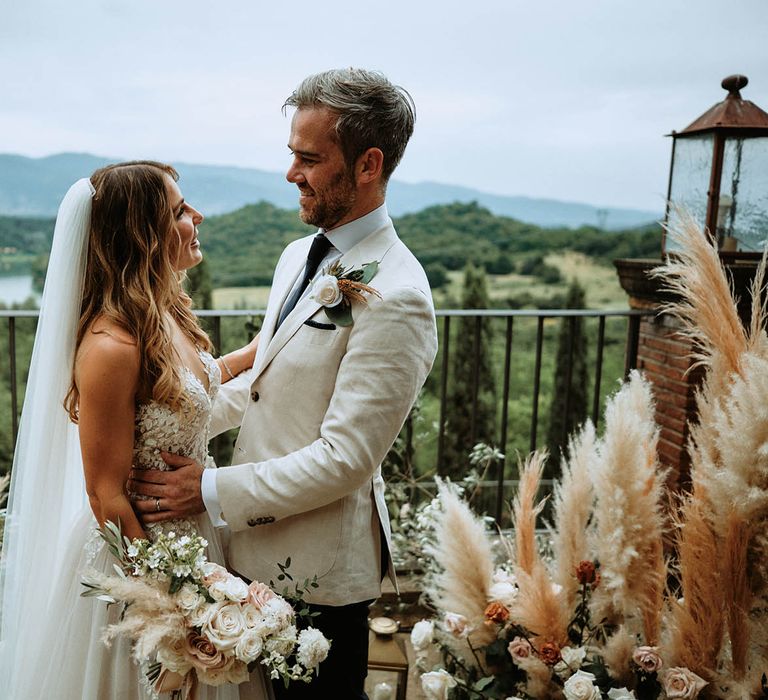 Bride and groom embrace at altar surronded by pampas grass decor and lanterns at destination wedding in Italy