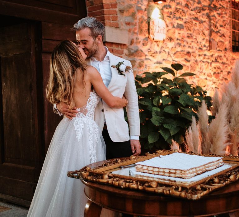 Bride and groom share a kiss next to wedding cake at destination wedding in Tuscany