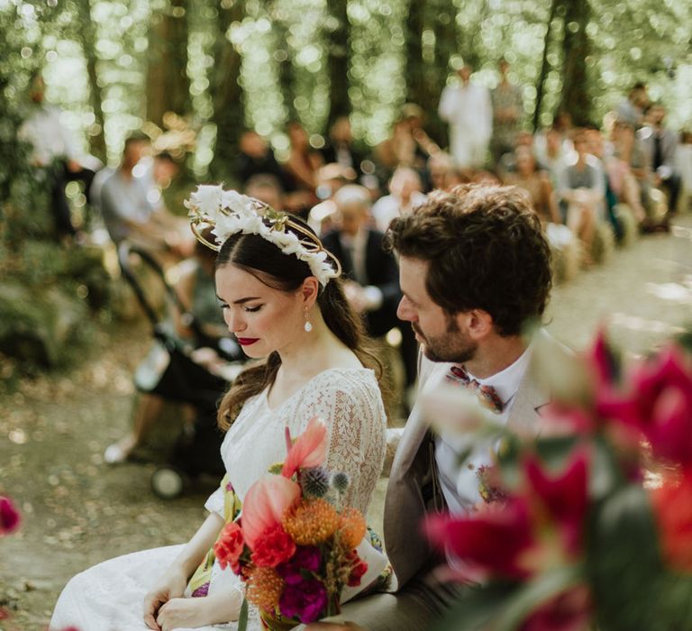 Bride in boho bridal crown and groom in griege suit sitting down during their wedding ceremony in Italy 