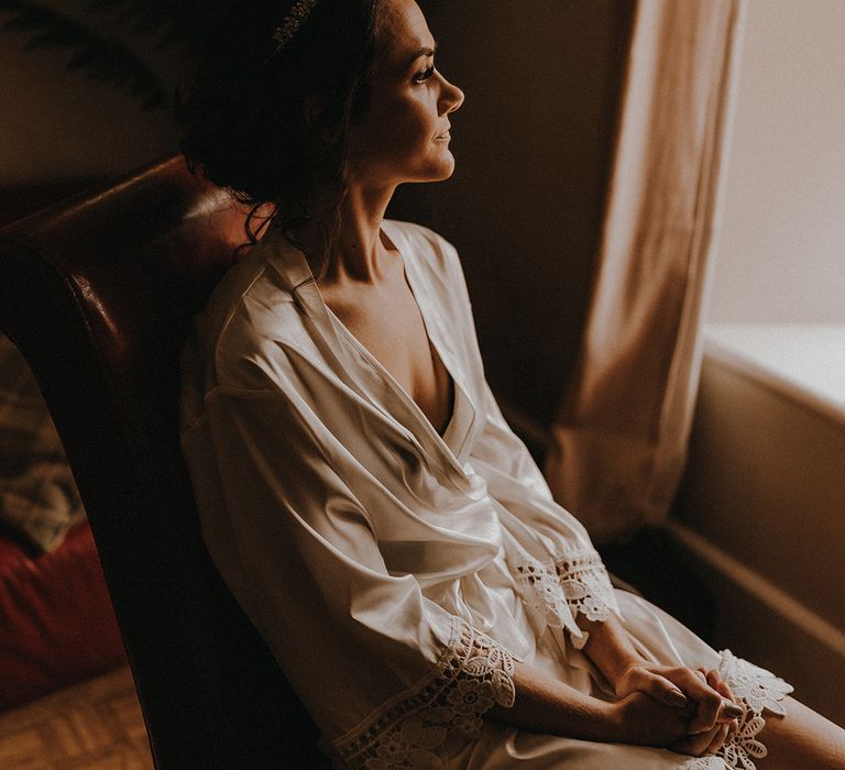 The bride wearing her sparkly wedding tiara sitting in a white bridal satin robe as she gets ready for the wedding 