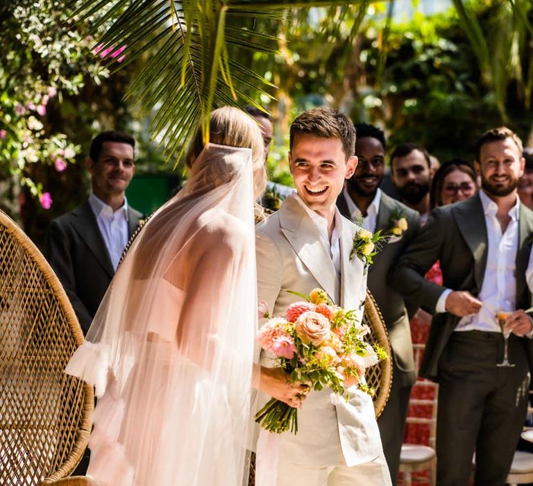 Groom in cream wedding suit smiling with the bride wearing a ruffle layer wedding veil for their wedding with a citrus colour scheme 