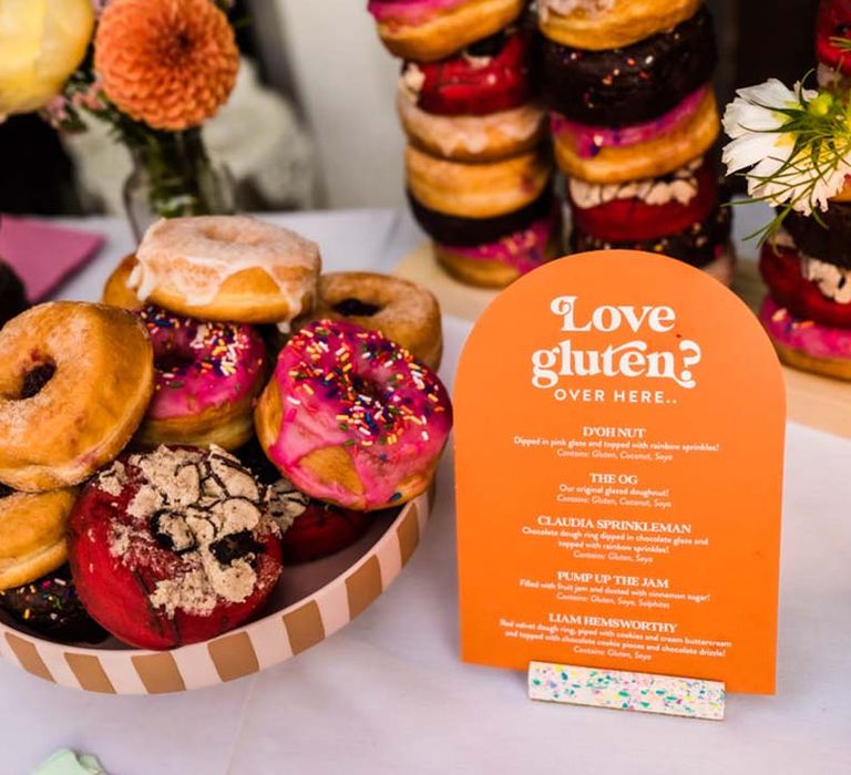 Orange and white arched doughnut menu sign with the bowls full of doughnuts for the wedding dessert 