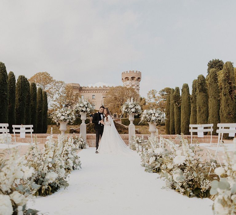 Bride and groom at the end of the aisle with white carpet and carnation, eucalyptus and dried flower aisle flower decorations with church wedding venue in Barcelona behind them 