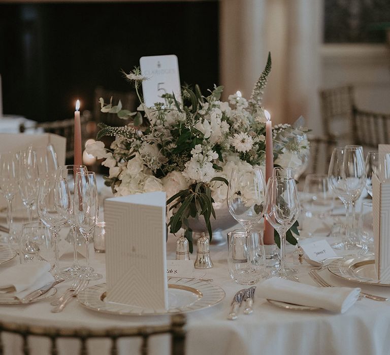 Neutral wedding tablescape with white table cloths, napkins, candles and more with table number sign and menu cards 