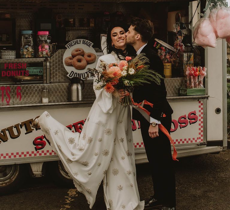 Doughnut van by the coast for lighthouse wedding with the bride and groom sharing a kiss in front of it 