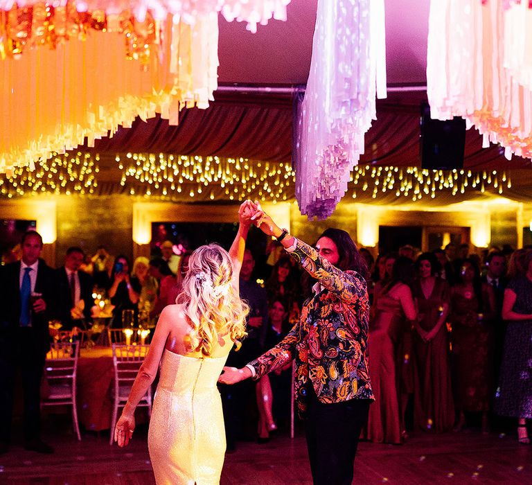 Bride in strapless sequin feather wedding reception dress having first dance with groom in neon patterned suit 