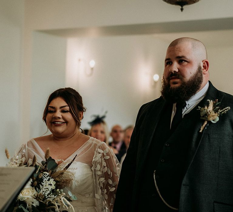 Groom in green tweed wedding suit with the bride in a lace long sleeve wedding dress at modern wedding 