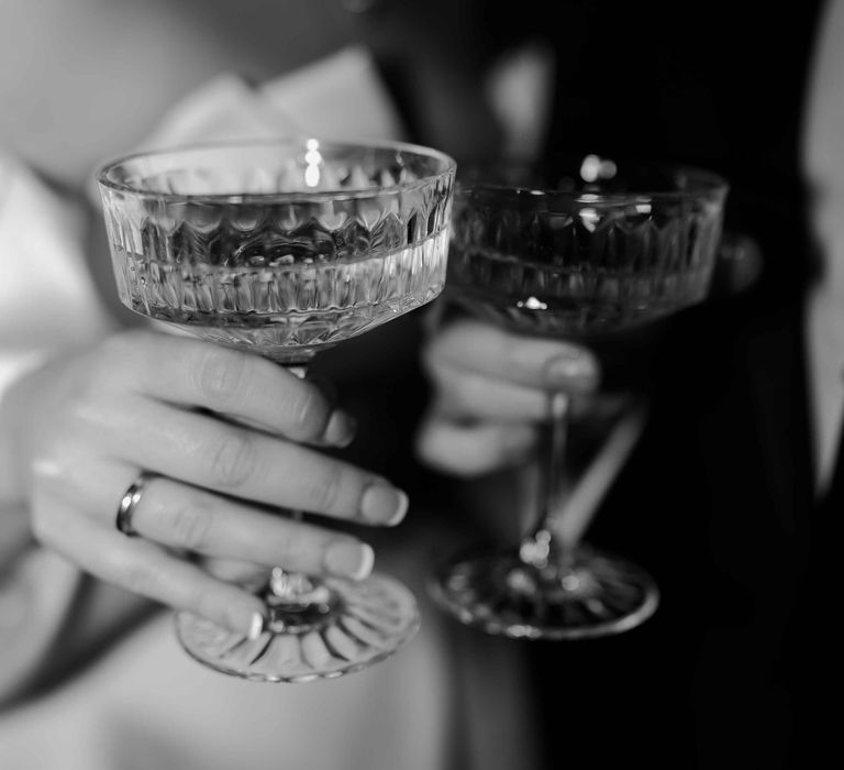 Bride shows off wedding ring and french tip wedding nails while holding a champagne coupe from the champagne tower