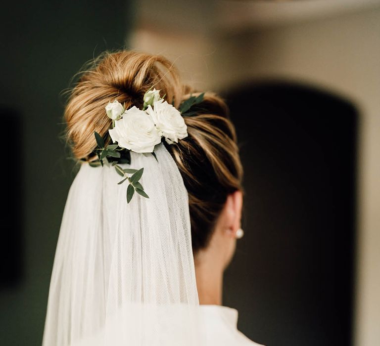 Bride with white rose floral hair accessory attached to bun hairstyle with white veil 