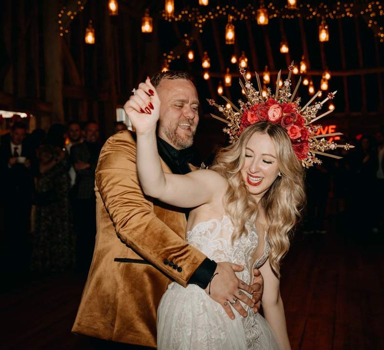 Groom in crushed velvet burnt orange grooms blazer and dried flower boutonniere dancing with bride in off shoulder lace wedding dress with corset style top and red rose and gold halo bridal crown at Southlands Barn 