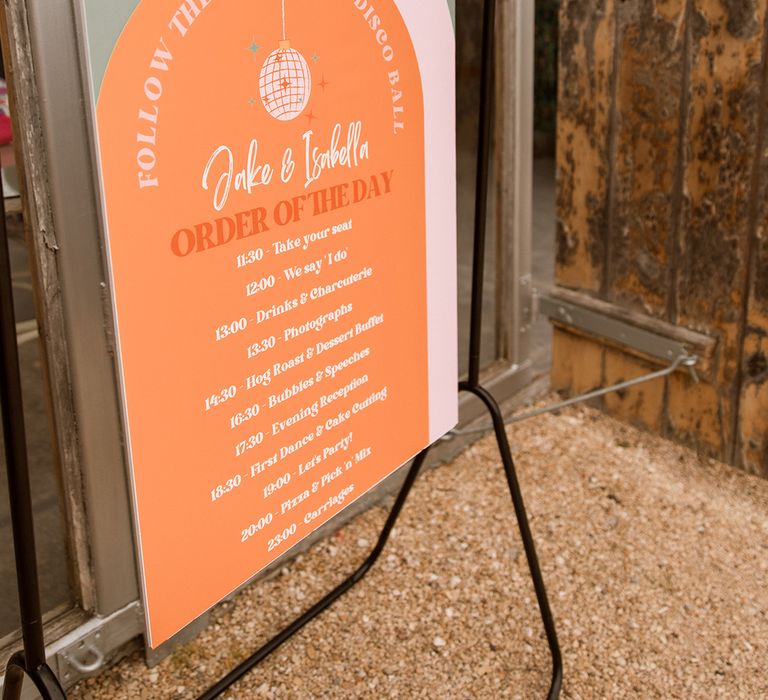 Orange order of the day wedding sign tied with orange ribbon onto the black frame 