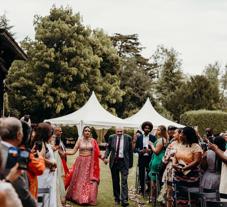 Father of the bride walks the bride down the aisle lined with autumnal leaves 