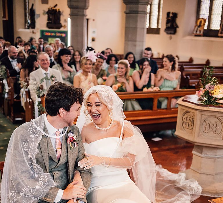 The bride and groom laugh heartily at their church wedding ceremony 