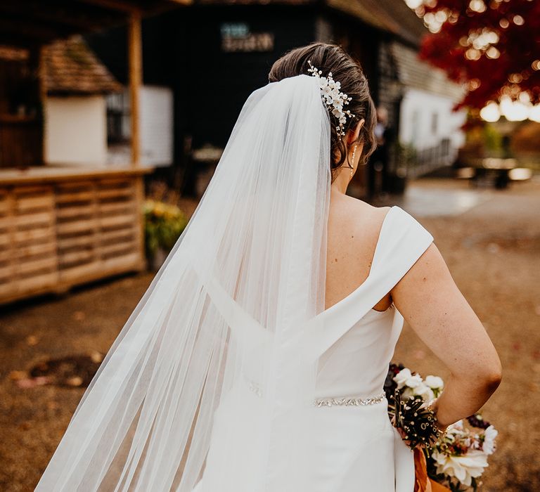 Bride wearing a bespoke custom wedding dress with her veil blowing in the breeze 