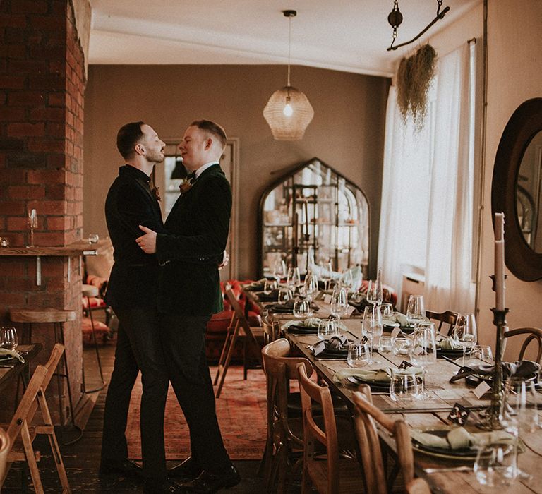 Industrial style Yorkshire wedding venue with the two grooms wearing velvet suit jackets embracing each other 