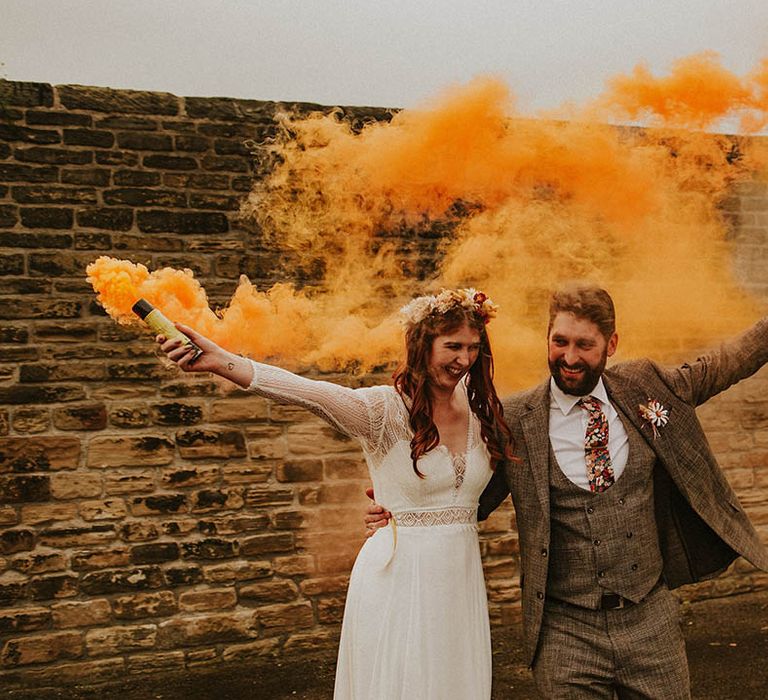 Wedding photo of the bride and groom waving around orange smoke bomb for autumnal wedding 