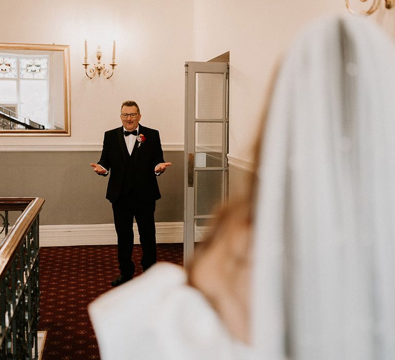 Father of the bride waits at the end of the hallway as he sees the bride for the first time 