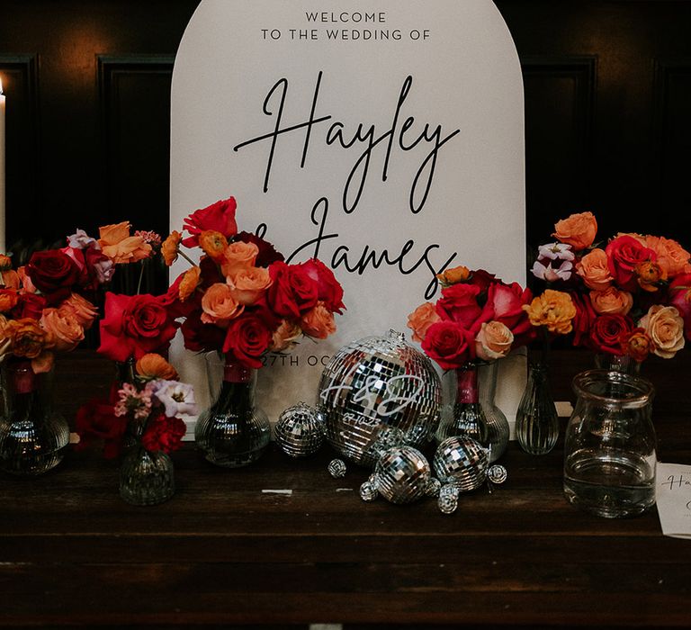 Black and white monochrome wedding welcome sign decorated with bright red and orange wedding flowers 