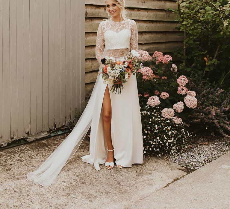 Bride in Catherine Deane wedding dress separates with lace top and side slit skirt holding an orange dahlia wedding bouquet by Steph Newton Photography