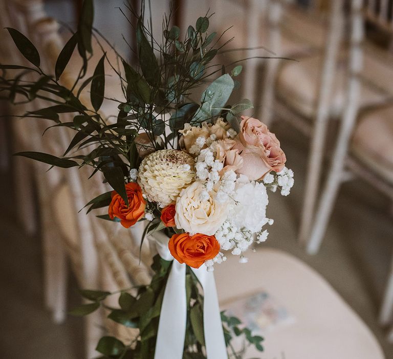 Autumnal floral decorations tied to the wedding chairs with ribbon 